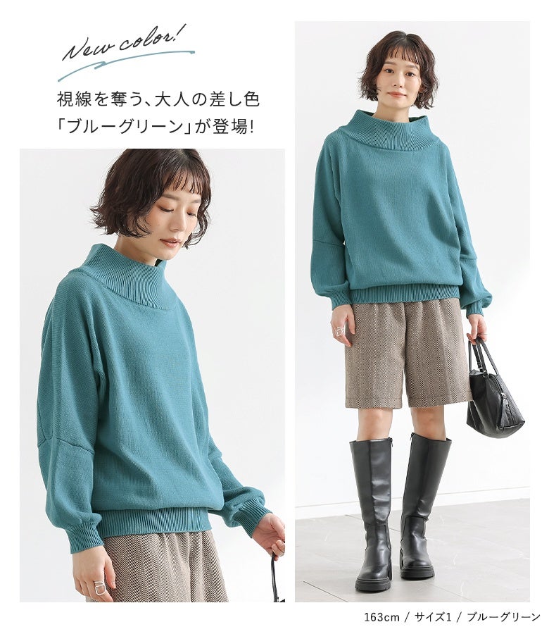 鮮やかなブルーグリーンの長袖綿ニットにチェック柄ショートパンツと黒のロングブーツを合わせた、大人の華やか秋コーデ。