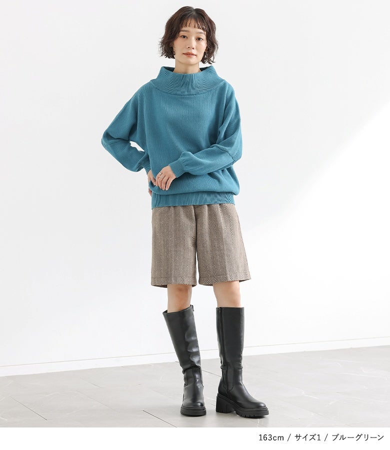 綺麗なブルーグリーンの綿ニットにチェック柄ショートパンツと黒のロングブーツを合わせた、トラッドで洗練された大人のお出かけスタイル。