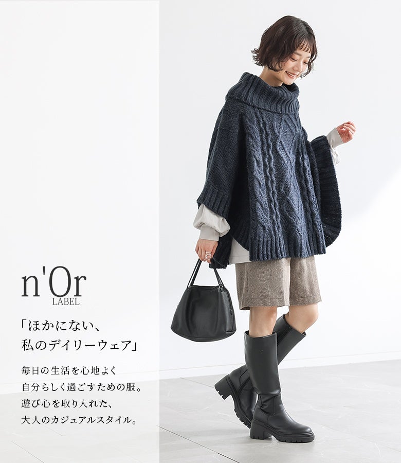 グリーンカラーのケーブル編みニットポンチョ。オフホワイトのブラウスをインナーに重ねることで、袖口や裾から覗く異素材のニュアンスが映え、お洒落度の高いレイヤードが完成します。