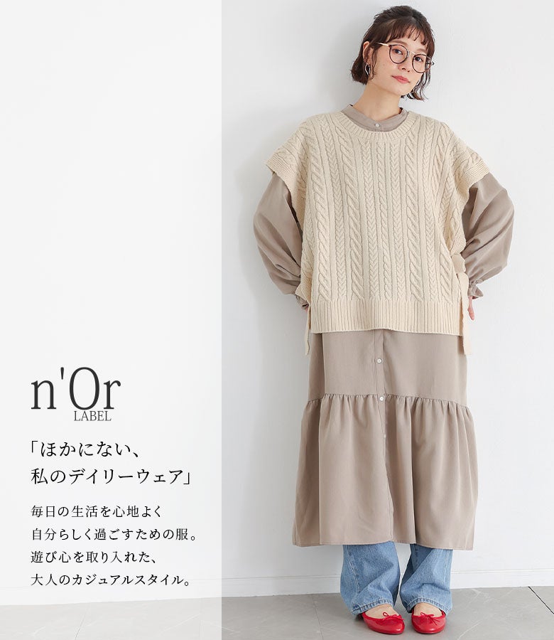 アイボリーのケーブルニットベストとグレージュのティアードワンピースに、デニムパンツと赤パンプスを組み合わせた、休日のお散歩やカフェ巡りにぴったりの大人カジュアルスタイル。
