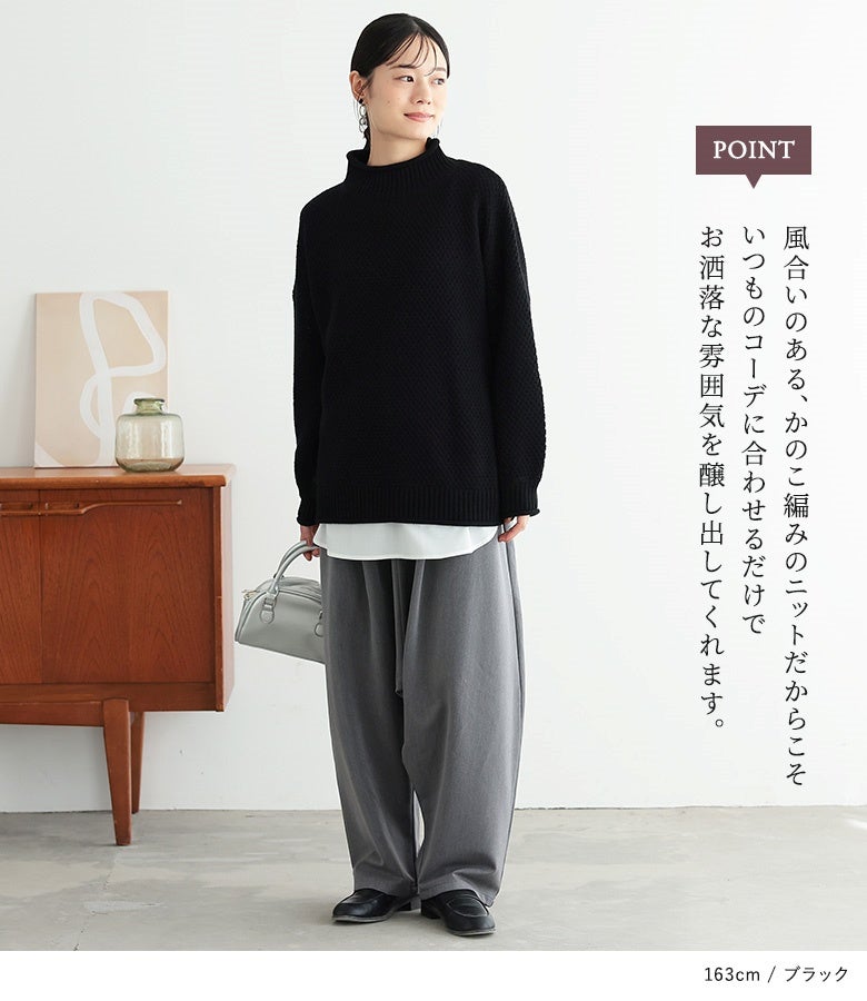 ブラックのかのこ編みハイネックニット。風合いのある黒の凹凸編地とゆったりとした裾ラインが、グレーのワイドパンツと合わせた大人のラフモードな装いを品よく引き締めます。