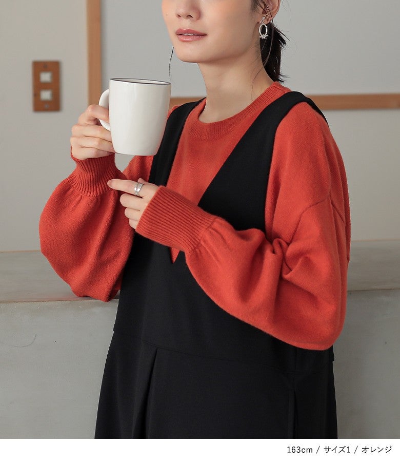 オレンジのぽわん袖パフスリーブニット。暖かみのある華やかなオレンジカラーと長めの袖リブ仕立てが、黒のジャンパースカートとの重ね着に旬のメリハリと可愛らしさを添えます。