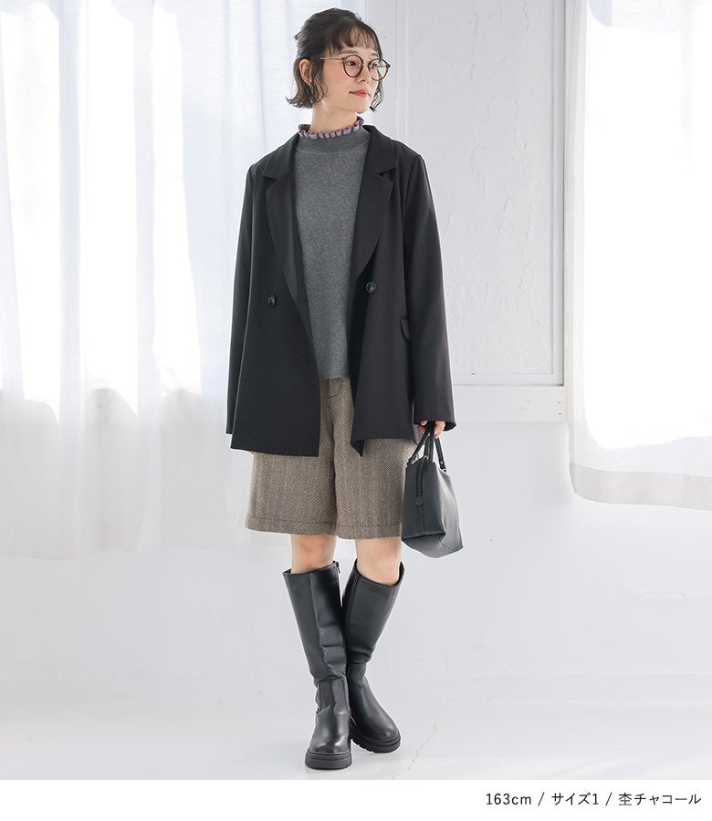 杢チャコールのフリルリブニットに黒のテーラードジャケット、ショートパンツ、ロングブーツを合わせたマニッシュ＆フェミニンな秋冬オフィスコーデ。
