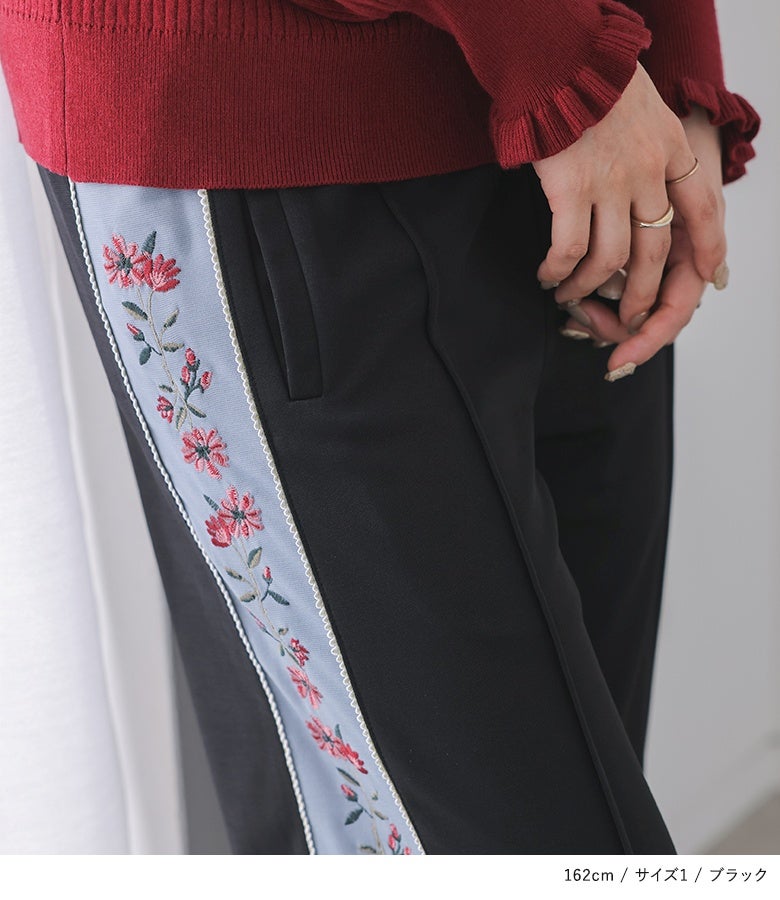 ブラックのジャージ生地に映えるライトブルーの配色テープと繊細なレッドの花柄刺繍。両サイドポケット付きで実用性にも優れたデザインボトムスです。