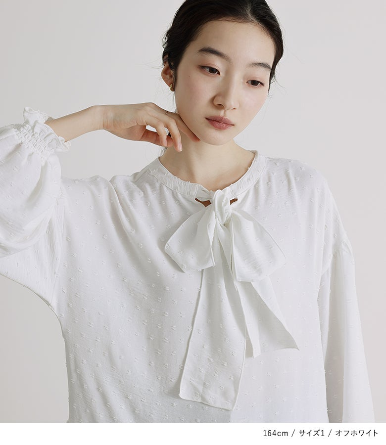 オフホワイトのドットジャガード前後2wayチュニックブラウス。表面感のあるカットドット生地と胸元のボウタイリボンが、顔周りをパッと明るく可憐な印象に魅せてくれます。