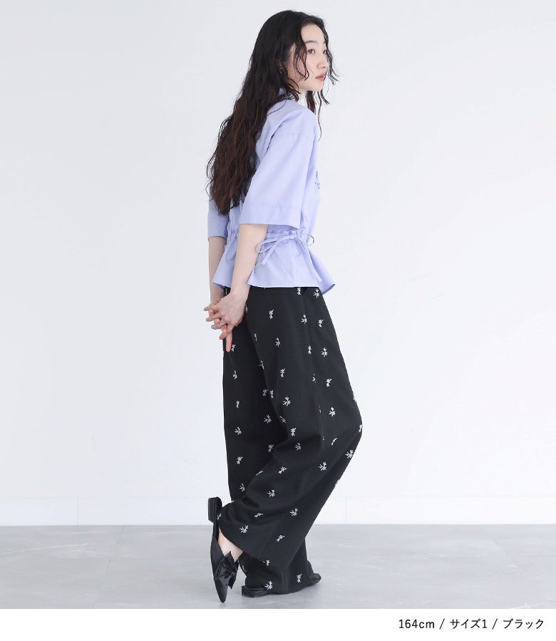ブラックの刺繍ストレートワイドパンツにパープルのシャツを合わせた着こなし。シックな黒地の小花刺繍と落ち感のあるシルエットが、サイドからの佇まいも華やかに魅せます。