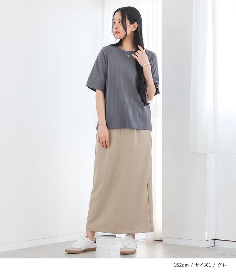 グレーの半袖リブカットソーにベージュのマキシ丈ロングスカート、白スニーカーを合わせた、大人のラフな春夏コーディネート。背面の裾スリットデザインが、バックスタイルまで手抜き感のないお洒落を演出。