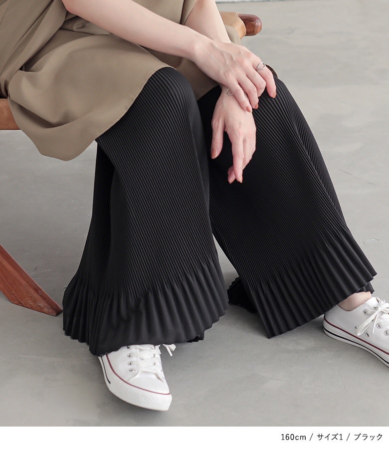 ブラックのペチワイドパンツ。膝下から広がる細やかなプリーツデザインが、スニーカーを合わせた足元に程よいボリュームと華やかなフリルラインを醸し出します。