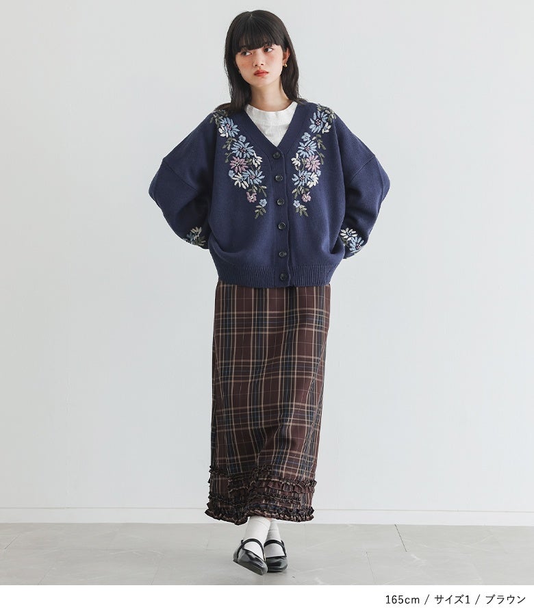 ブラウンのジャンパースカートに花刺繍ニットカーディガンを重ねたスタイル。裾から覗くフリルとチェック柄が、ニットの重たさを軽減し華やかなアクセントを添えます。