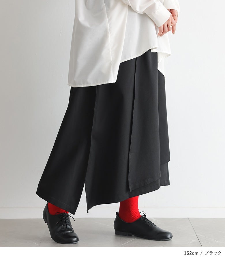 ブラックの変形ラップパンツにオーバーサイズの白シャツを合わせたモノトーンモードスタイル。広がりすぎないワイドシルエットとラップデザインが洗練された足元を作り出し、オフィスカジュアルや街歩きにおすすめです。