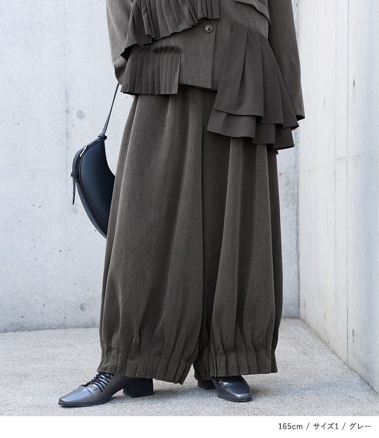 グレーの裾シャーリングタックワイドパンツ。裾の繊細なギャザー仕立てが足元に程よい重厚感を与え、マニッシュなレザーシューズやブーツとも好相性に決まります。