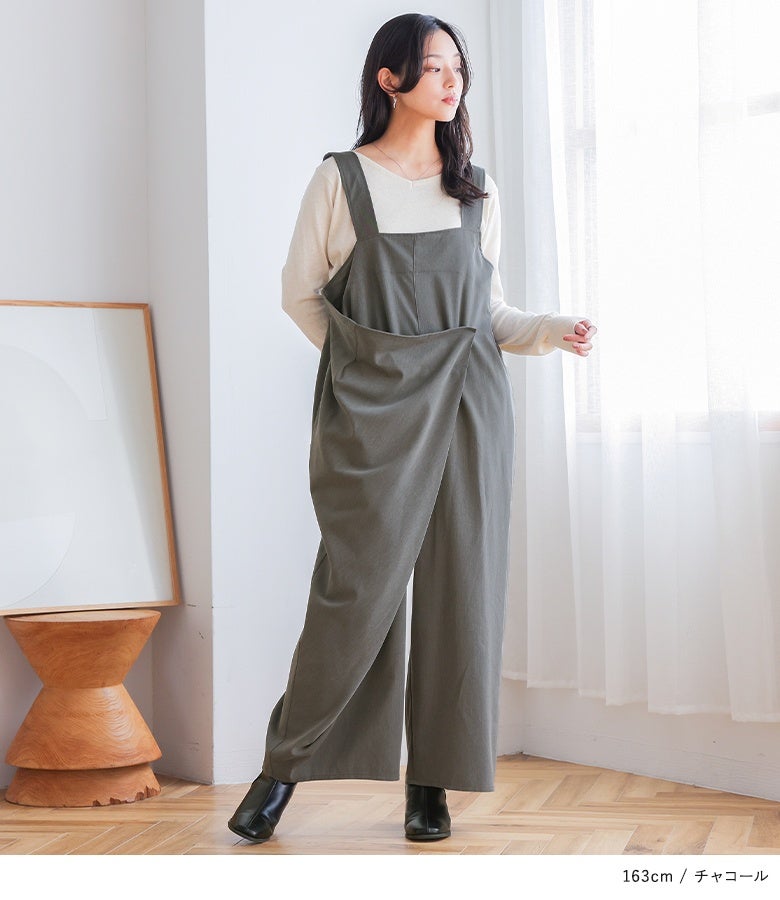 チャコールのアシメラップサロペット。裾までストンと落ちる広がりすぎないストレートワイドフォルムが、動きやすさとすっきりとしたスタイルアップ効果を同時に与えます。