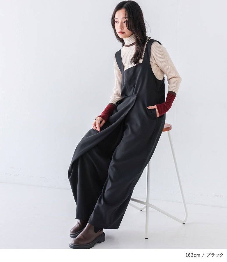 ブラックのアシメラップサロペットにハイネックニットを合わせた着こなし。深みのある黒地に際立つラップ風のドレープラインが、着こなし全体を上品でシックな印象へ導きます。