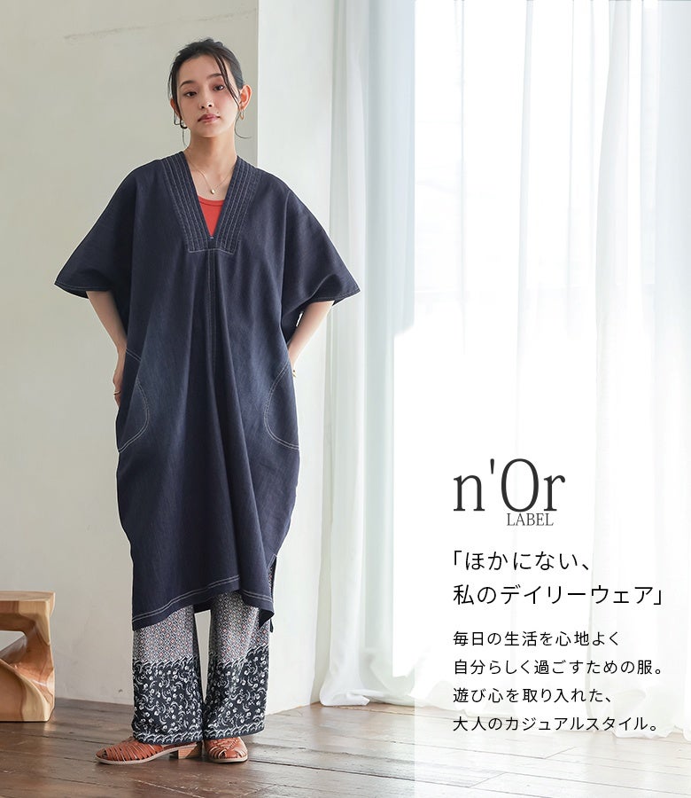 インディゴカラーの半袖デニムカフタンワンピースに総柄ワイドパンツを重ねた、オリエンタルな雰囲気漂う大人のリゾート風レイヤードコーデ。