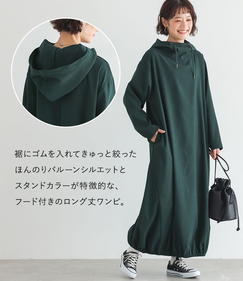 ダークグリーンのフード付きバルーンロングワンピースに黒のスニーカーと巾着バッグを合わせた大人カジュアルコーデ。裾絞りデザインとスタンドカラーで、肌寒い季節のお出かけや行楽シーンにもぴったりです。