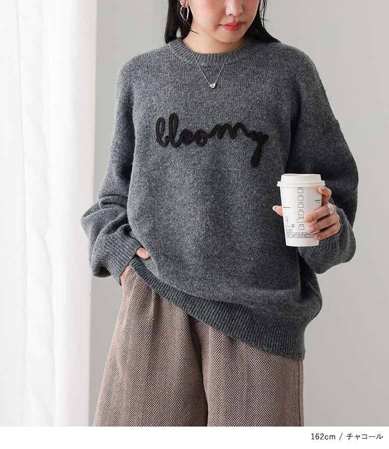 胸元に立体的なコード刺繍ロゴがあしらわれたチャコールカラーのニットトップス。ゆったりとしたシルエットで、ヘリンボーン柄のワイドパンツと合わせた大人のリラックスカジュアルスタイルです。