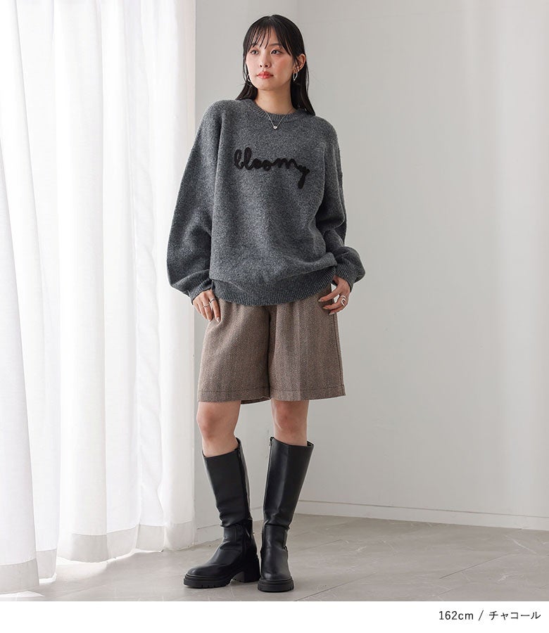 チャコールカラーの立体ロゴ刺繍ニットに、ツイード調ショートパンツと黒のロングブーツを合わせたコーディネート。ゆったりとしたシルエットのトップスが抜け感を演出します